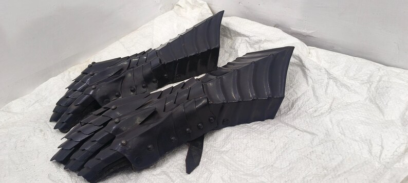 May include: A pair of black leather gauntlets with a scaly, armored design. The gauntlets are made of overlapping plates that create a textured surface.