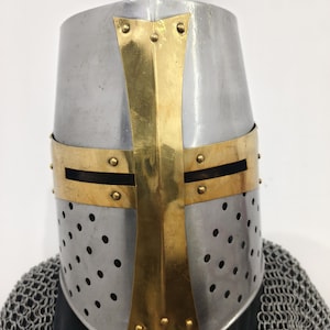 May include: A silver and gold crusader helmet with a cross design. The helmet has a perforated metal faceplate and a pointed top.