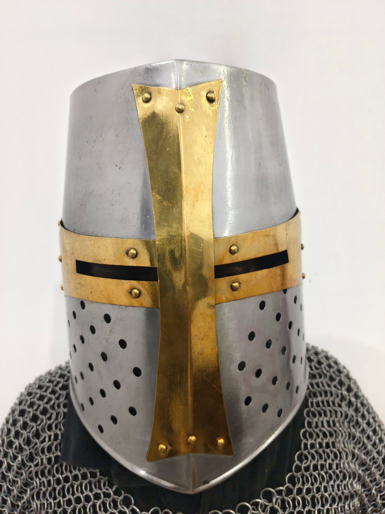 May include: A silver and gold crusader helmet with a cross design. The helmet has a perforated metal faceplate and a pointed top.