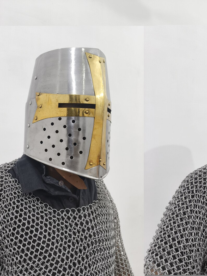 May include: A silver helmet with a gold cross design. The helmet has a mesh design and is worn by a person wearing chainmail.