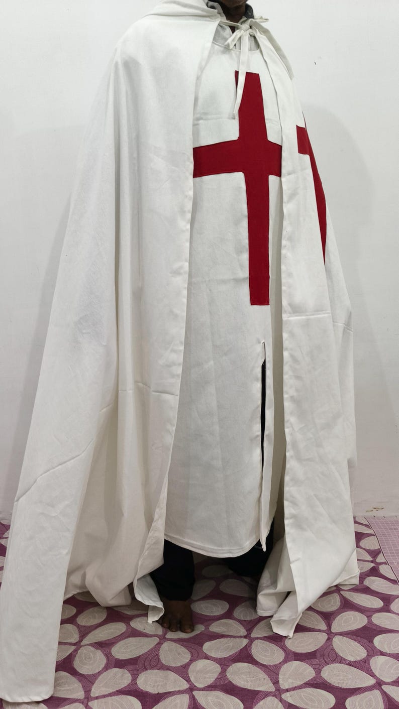 Op de afbeelding: Een witte kapmantel met een rood kruis op de voorkant. De mantel wordt gedragen door een persoon, maar de persoon is niet zichtbaar op de afbeelding.