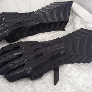 May include: A pair of black leather gauntlets with a scaly design. The gauntlets are made of thick leather and have a medieval look.