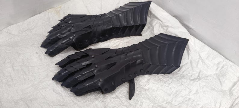May include: A pair of black leather gauntlets with a scaly design. The gauntlets are made of thick leather and have a medieval look.