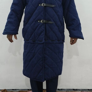 May include: A long, quilted, navy blue coat with a high collar and multiple buckles. The coat is made of a thick, durable fabric and has a diamond-shaped quilting pattern.
