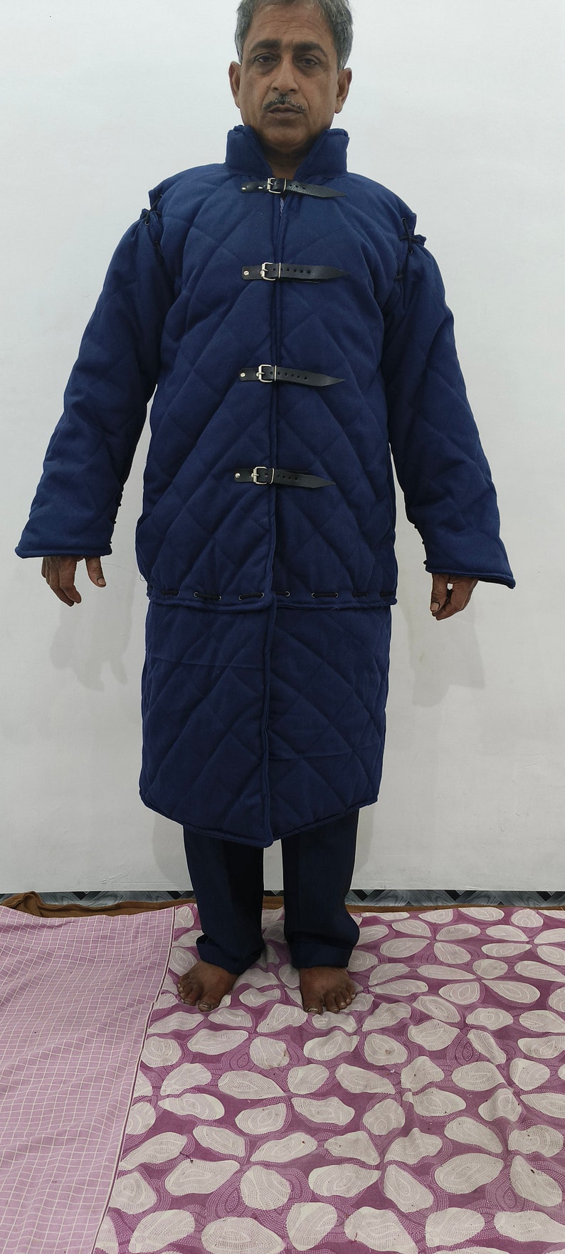 May include: A long, quilted, navy blue coat with a high collar and multiple buckles. The coat is made of a thick, durable fabric and has a diamond-shaped quilting pattern.