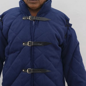 May include: A blue quilted jacket with a high collar and multiple leather straps and buckles. The jacket is made of a thick, durable fabric and has a diamond-shaped quilting pattern.