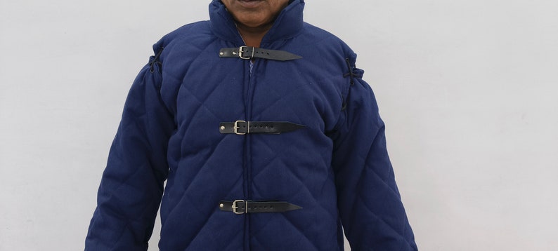May include: A blue quilted jacket with a high collar and multiple leather straps and buckles. The jacket is made of a thick, durable fabric and has a diamond-shaped quilting pattern.