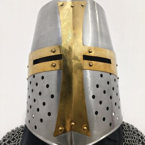May include: A silver helmet with a gold cross design and a perforated metal surface. The helmet is a traditional crusader helmet.