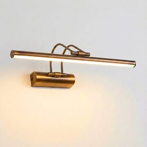Peut inclure: Un éclairage de tableau de couleur bronze. Le luminaire est composé d'une longue barre horizontale avec une lumière LED intégrée. Le luminaire est fixé au mur et possède une base cylindrique et des bras réglables.