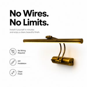 May include: A brass-toned picture light with a horizontal cylindrical lamp head and two curved support arms attached to a rectangular wall-mount base. Text reads: No Wires. No Limits. Install it yourself in minutes and enjoy a clean, beautiful finish.