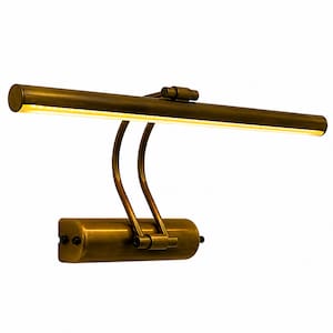 May include: A wall-mounted picture light with an antique brass finish. The fixture features a horizontal cylindrical lamp head with an integrated LED light strip, connected by two curved metal arms to a rectangular base with two side screws.