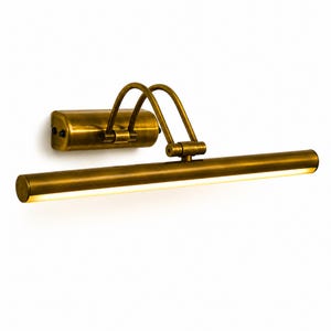 May include: A wall-mounted picture light with an antique brass finish. The fixture features a rectangular base, two curved support arms, and a long, cylindrical horizontal lamp head with an integrated light strip emitting a warm glow.