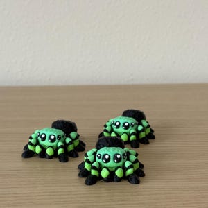 May include: Three small spider figurines featuring a bright lime green and black striped pattern. Each spider has a rounded body, eight legs, and large, glossy black eyes with white highlights, creating a detailed and textured appearance.