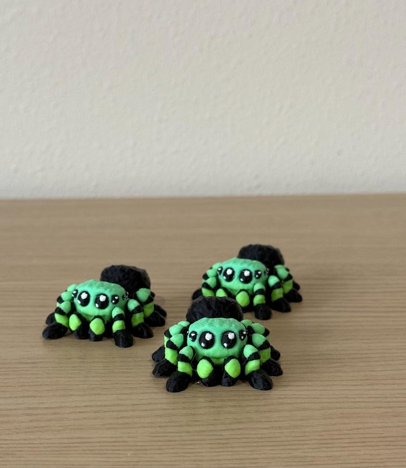 May include: Three small spider figurines featuring a bright lime green and black striped pattern. Each spider has a rounded body, eight legs, and large, glossy black eyes with white highlights, creating a detailed and textured appearance.
