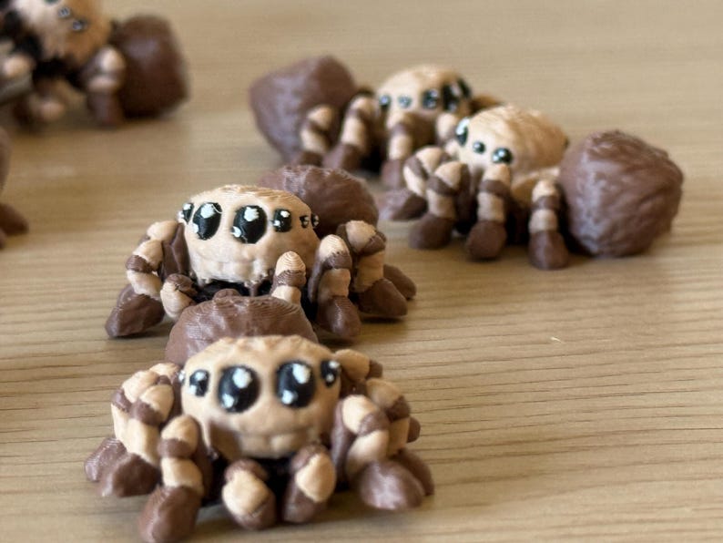 May include: A collection of small, sculpted spider figurines featuring tan and dark brown striped legs, a rounded tan head with large black eyes, and a solid dark brown abdomen. Each spider is crafted with a smooth, matte finish and detailed texture.