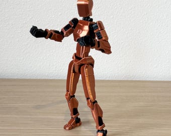 May include: A posable action figure with a metallic copper finish and black joints. The figure features a smooth, rounded head, articulated limbs, and the number 13 embossed on the center of the chest plate. It stands in a dynamic, forward-facing pose.