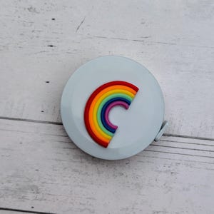 Puede incluir: Una cinta m&eacute;trica blanca con un dise&ntilde;o de arco&iacute;ris. El arco&iacute;ris est&aacute; hecho de rojo, naranja, amarillo, verde, azul, a&ntilde;il y violeta.