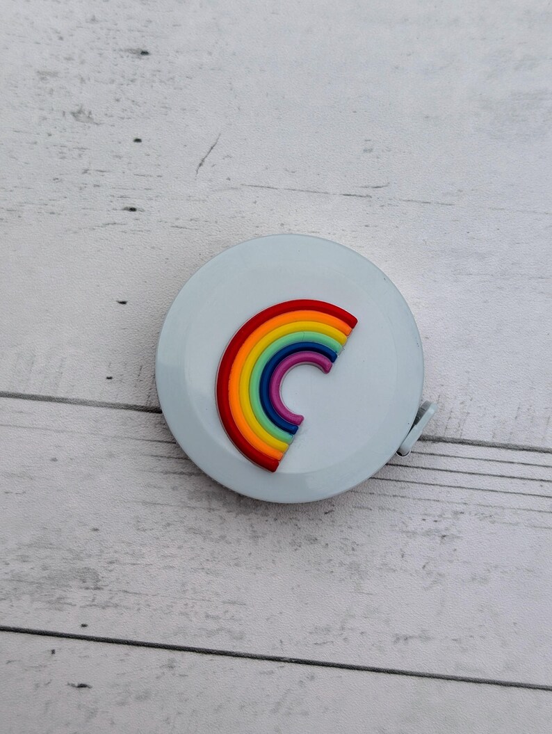 Puede incluir: Una cinta m&eacute;trica blanca con un dise&ntilde;o de arco&iacute;ris. El arco&iacute;ris est&aacute; hecho de rojo, naranja, amarillo, verde, azul, a&ntilde;il y violeta.