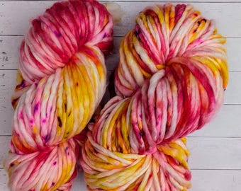 May include: Two skeins of chunky yarn in a bright color combination of pink, yellow, and white. The yarn is hand-dyed and has a unique, speckled look.