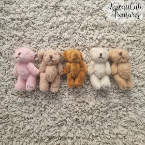 May include: Five small teddy bears in different colours: pink, cream, brown, white, and beige. The bears are lying on a white fluffy surface. The text "KawaiiCute Treasures" is visible at the top of the image.