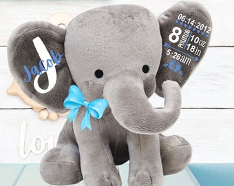 May include: A plush gray elephant toy featuring a bright blue bow around its neck. The left ear displays the name Jacob in white and blue, while the right ear shows birth details: 06.14.2012, 8 pounds 10 oz, 18 in, and 5:26 am.