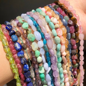 Könnte beinhalten: Eine Sammlung bunter Edelsteinperlen, darunter Amethyst, Türkis, Lapislazuli und Rosenquarz. Die Perlen sind auf einer Schnur aufgefädelt und bereit für die Schmuckherstellung.