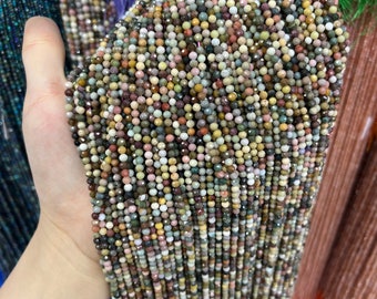May include: A strand of multi-colored gemstone beads. The beads are small and round, and they are strung on a thin wire. The beads are a mix of brown, green, pink, and white.