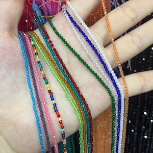 Op de afbeelding: Een selectie van kristal kralenstrengen in verschillende kleuren, waaronder blauw, groen, rood en paars. De strengen zijn waaiervormig op een hand gerangschikt.