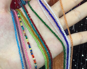 May include: A variety of crystal bead strands in different colors, including blue, green, red, and purple. The strands are arranged in a fan shape on a hand.