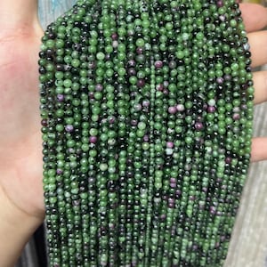 May include: A strand of green, black, and pink gemstone beads. The beads are round and have a smooth, polished finish.