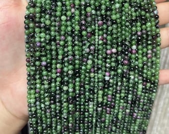 May include: A strand of green, black, and pink gemstone beads. The beads are round and have a smooth, polished finish.