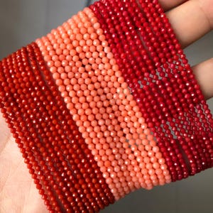 Op de afbeelding: Close-up van meerdere strengen kleine, gefacetteerde kralen in verschillende tinten rood en koraal. De kralen zijn uniform van grootte en vorm. Ideaal voor het maken van sieraden of knutselprojecten.
