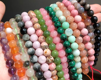 May include: A collection of colorful gemstone beads, including green, pink, and black, arranged in rows. The beads are round and smooth, and they are perfect for making jewelry.