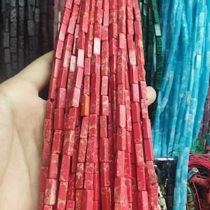 May include: A strand of red and white rectangular gemstone beads. The beads are made of a natural stone with a marbled pattern.