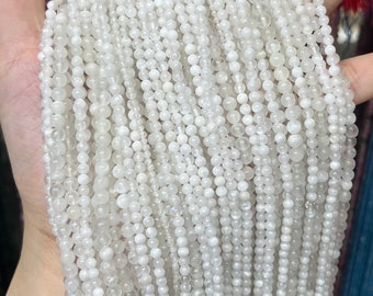 May include: Strands of white, round beads of varying sizes are held in a hand. The beads have a pearlescent sheen and appear to be strung together. The beads are likely for jewelry making or crafting.
