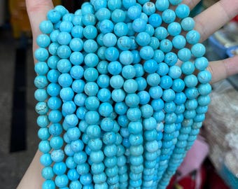 May include: A collection of round, light blue turquoise beads. The beads are strung together, creating a flowing, textured appearance. The beads are a consistent size and shape, with a slightly matte finish.