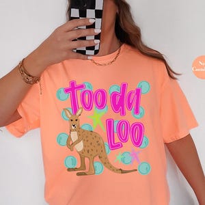 May include: Neon cantaloupe-colored t-shirt with the text "Tooda Loo" in pink, a cartoon kangaroo, and blue bubble graphics. The shirt is a short-sleeved, casual style.