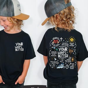 May include: A black t-shirt with the text "YOUR WAY'S BETTER" on the front and a graphic design on the back. The design includes text, a cross, a sun, and other illustrations. The child is wearing a trucker hat.