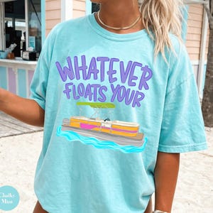 Peut inclure: T-shirt bleu clair avec l'inscription "WHATEVER FLOATS YOUR" en violet et un motif de bateau. Le t-shirt est de coupe ample et fabriqué dans une matière douce. Parfait pour une journée à la plage.