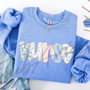 May include: A light blue sweatshirt with the word "nurse" spelled out in colorful patterned letters. The letters are made up of different floral and geometric patterns in pink, blue, and white.