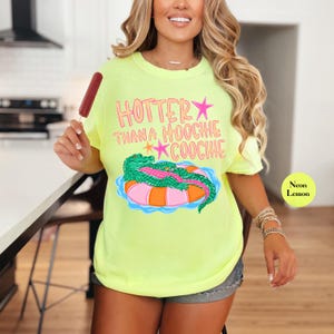 Puede incluir: Camiseta amarillo ne&oacute;n con el texto "Hotter Than a Hoochie Coochie" y un gr&aacute;fico de un caim&aacute;n en una boya. La camiseta es de color amarillo brillante y tiene un corte holgado.
