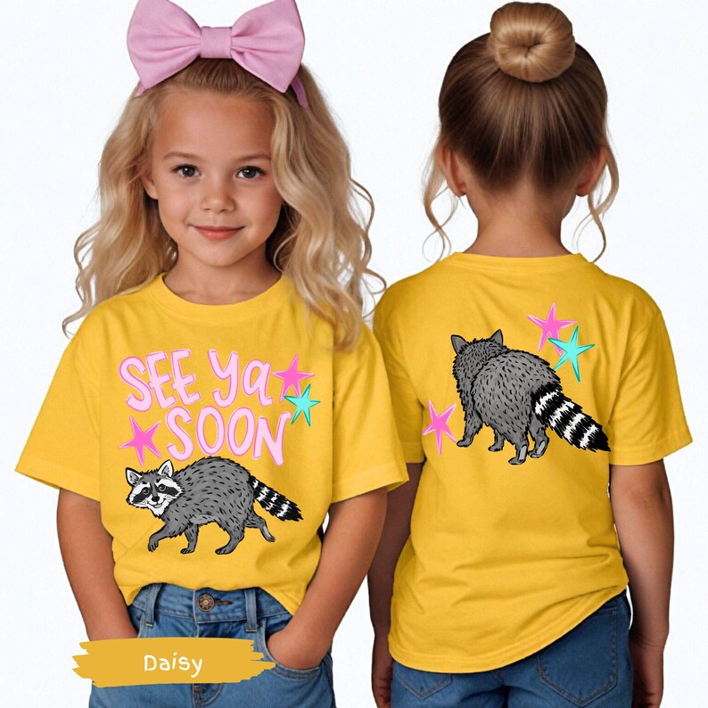 May include: Yellow t-shirts with a raccoon graphic and the text "SEE Ya SOON". The front of the shirt shows the raccoon walking, while the back shows the raccoon from behind. The shirts have pink and teal star accents.