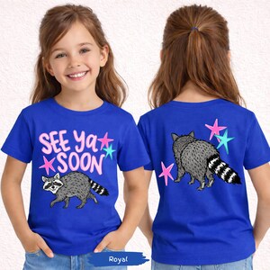 May include: Royal blue t-shirt featuring a raccoon graphic and the text "SEE YA SOON" in pink and blue. The back of the shirt also has a raccoon and star graphics. A fun and colorful design for kids.
