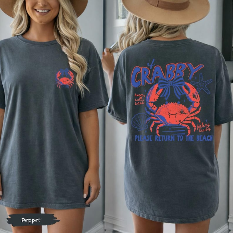 Puede incluir: Camiseta gris oscuro con un dise&ntilde;o de cangrejo en la parte delantera y trasera. La parte trasera presenta un gran gr&aacute;fico de cangrejo con el texto "It's Crabby" y "Please Return to the Beach". La camiseta tiene un corte holgado.