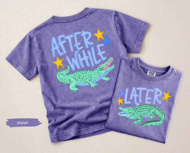 Puede incluir: Dos camisetas violetas con gr&aacute;ficos de caimanes. Una camiseta dice "AFTER WHILE" con un caim&aacute;n verde y estrellas amarillas y azules. La otra camiseta dice "LATER" con un caim&aacute;n verde y estrellas amarillas y azules.