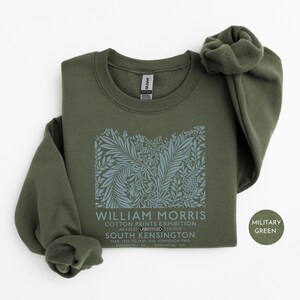 Puede incluir: Sudadera verde militar con un dise&ntilde;o floral y el texto "WILLIAM MORRIS COTTON PRINTS EXHIBITION". La sudadera tiene cuello redondo y mangas largas. El texto tambi&eacute;n incluye "SOUTH KENSINGTON".