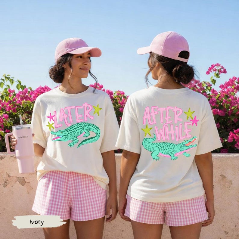 May include: Ivory-colored t-shirts with a cartoon alligator design and the words "LATER" and "AFTER WHILE" in pink. The shirts are paired with pink gingham shorts and a pink baseball cap. A pink tumbler is held in the left hand.