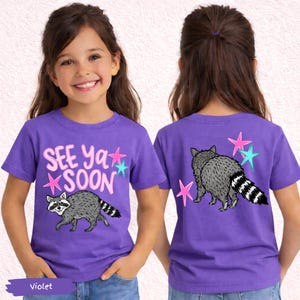 May include: Violet short-sleeve t-shirt with a raccoon graphic and the text "SEE Ya SOON". The design includes pink and teal stars. The back of the shirt also features a raccoon and stars.