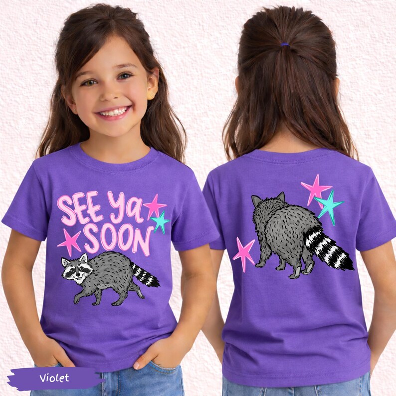 May include: Violet short-sleeve t-shirt with a raccoon graphic and the text "SEE Ya SOON". The design includes pink and teal stars. The back of the shirt also features a raccoon and stars.