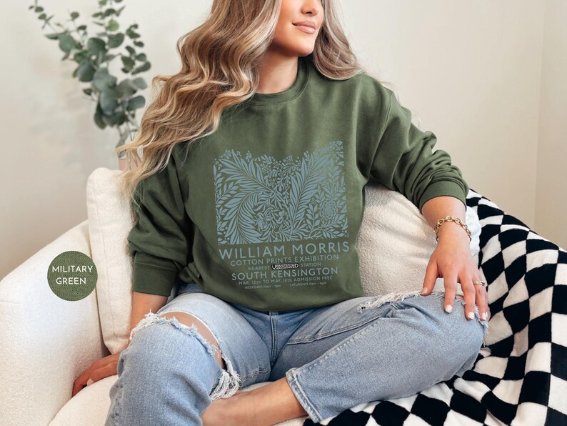 Puede incluir: Sudadera verde oliva con un dise&ntilde;o floral y el texto "WILLIAM MORRIS COTTON PRINTS EXHIBITION". La sudadera se combina con vaqueros azul claro. El estilo es informal y c&oacute;modo.